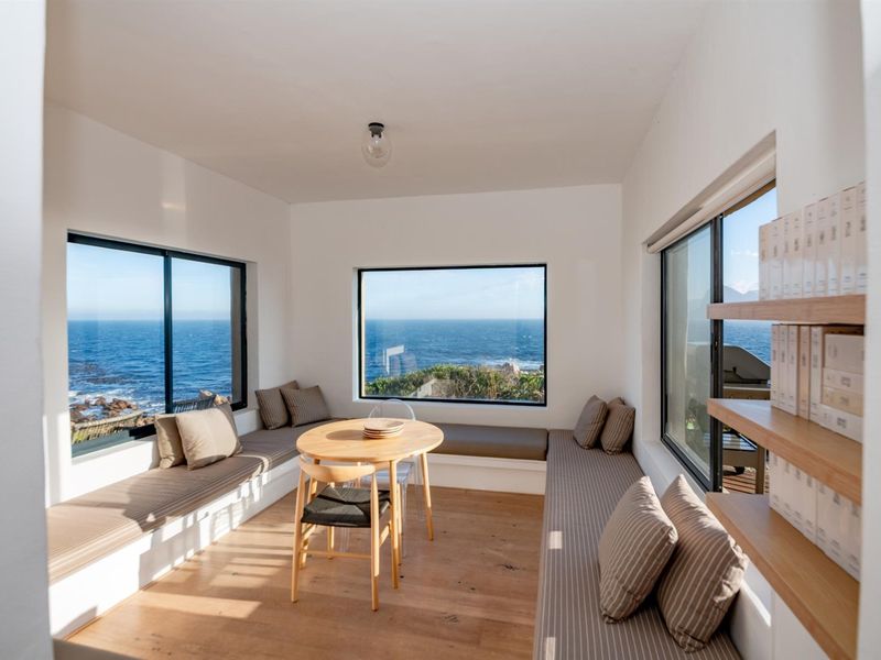 A bright living area featuring built-in bench seating, timber flooring, and expansive windows offering panoramic ocean views.