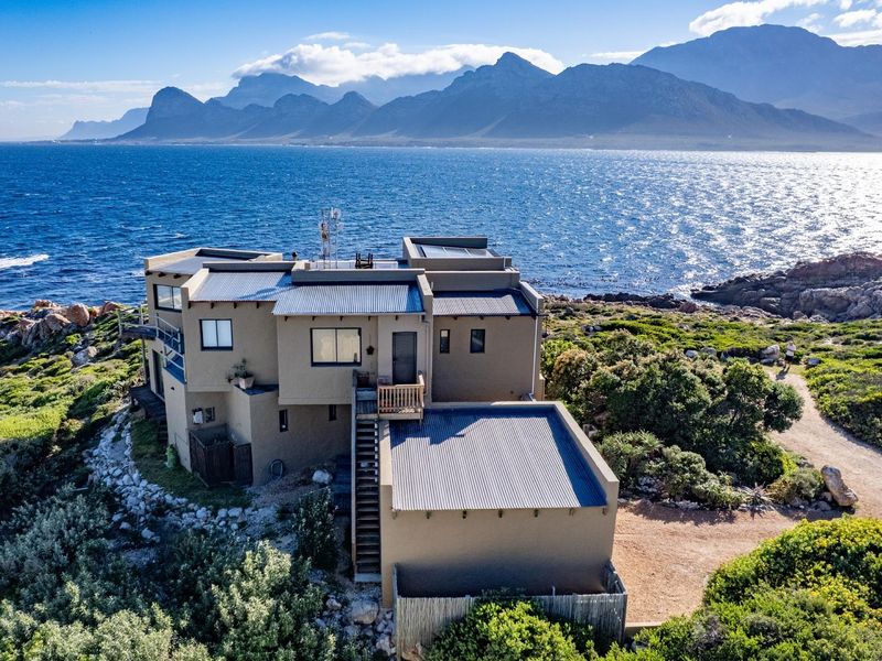 Aerial view of a coastal property featuring a multi-level design with corrugated metal roofing, solar panels, and expansive ocean and mountain views.