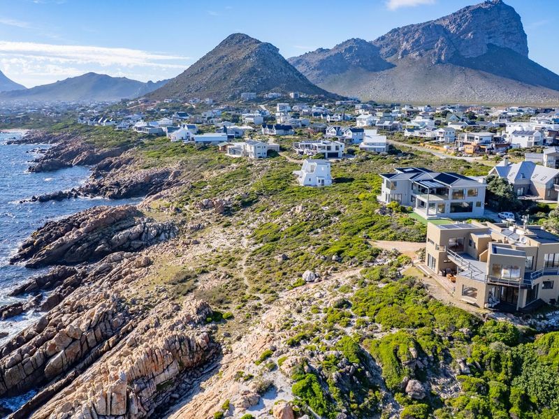 An aerial view of a coastal residential estate situated along a rocky shoreline with scenic mountain views.