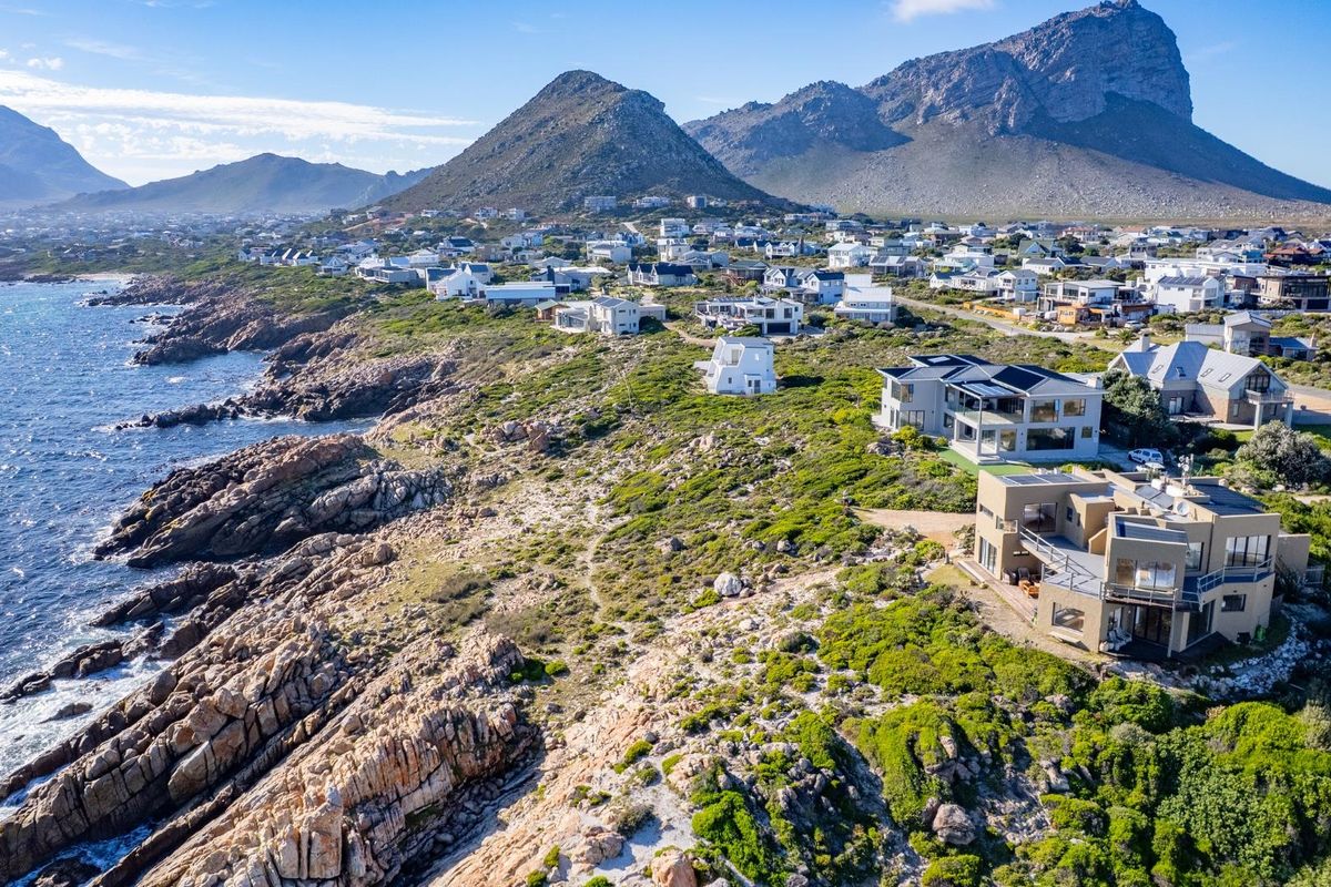 An aerial view of a coastal residential estate situated along a rocky shoreline with scenic mountain views.