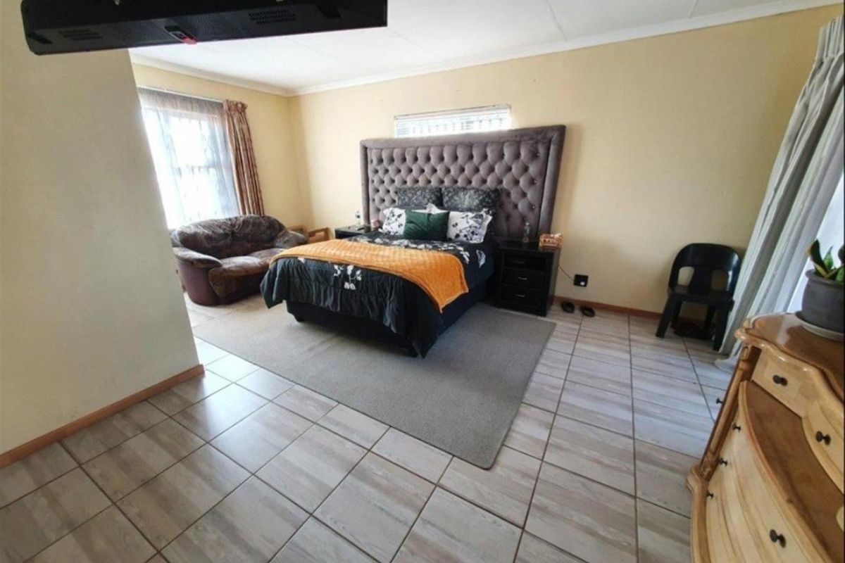 A spacious bedroom featuring neutral wall tones, tiled flooring, and a large window allowing for natural light.