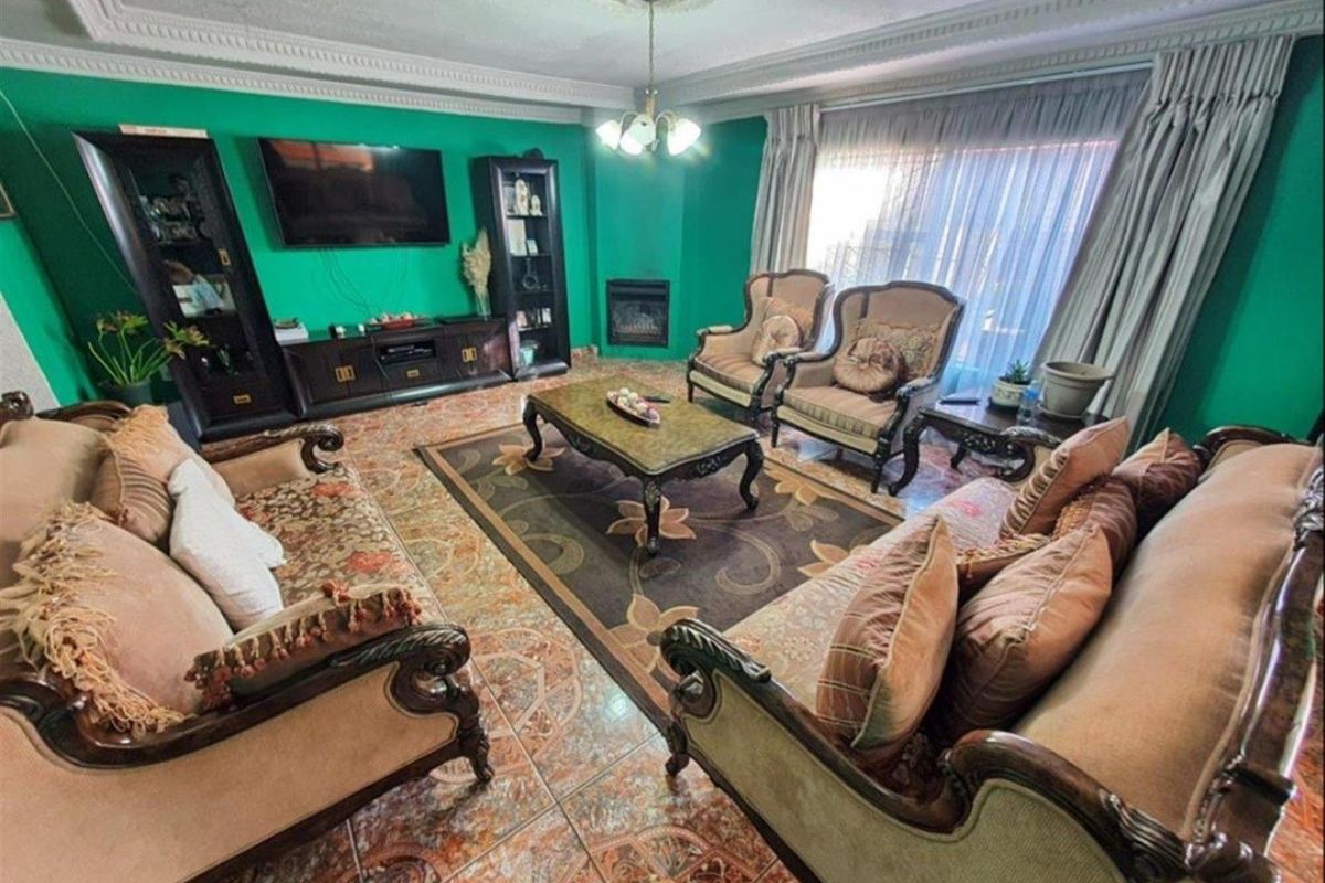 A spacious living room featuring decorative ceiling cornices, a built-in fireplace, and tiled flooring.