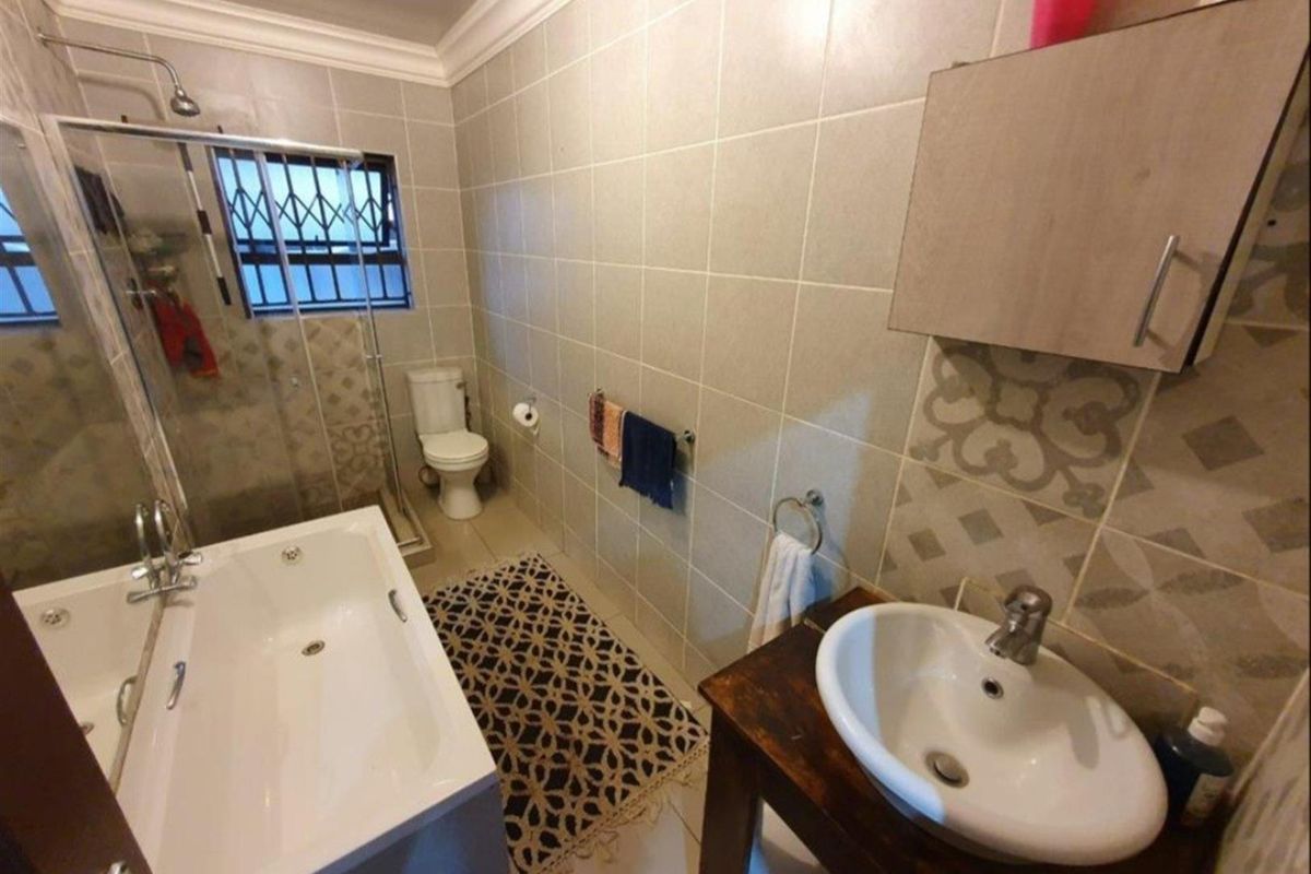 A functional bathroom featuring a built-in bathtub, a separate glass-enclosed shower, a toilet, and a vanity basin with wall-mounted cabinetry.