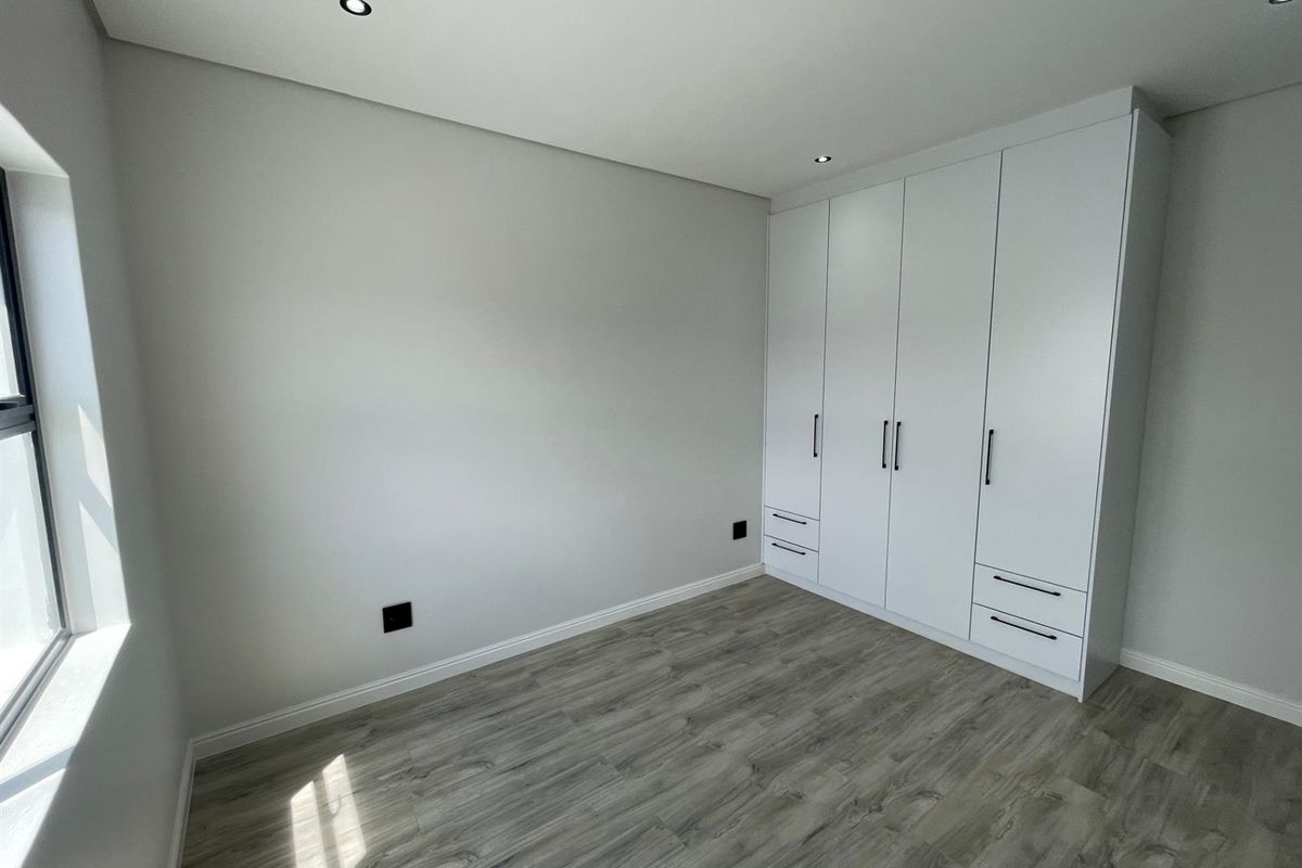 A bright, modern bedroom featuring neutral walls, high-quality laminate flooring, and ample built-in cupboard storage with recessed downlighting.