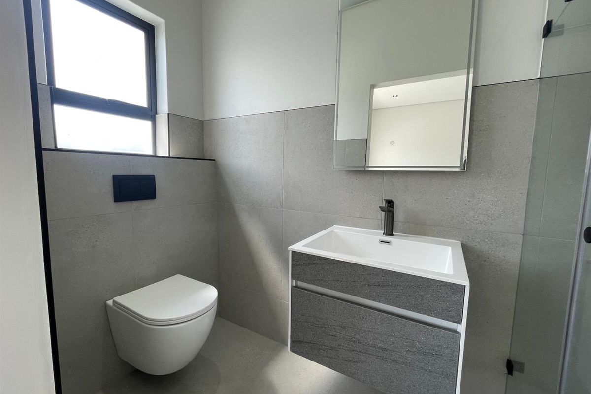 Modern bathroom featuring a wall-hung toilet, contemporary vanity with basin, and large wall mirror, finished with neutral grey tiling.