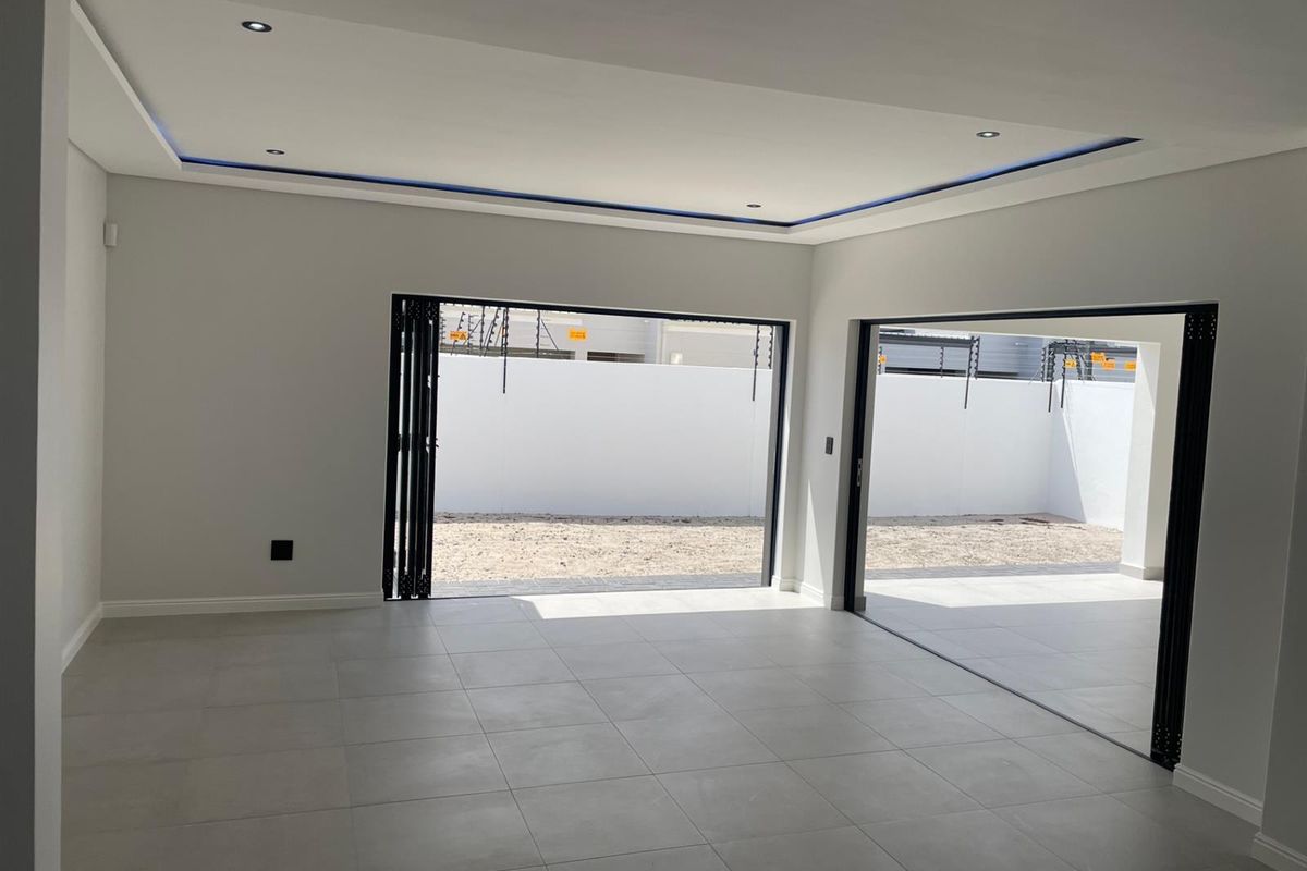 Spacious, modern living area featuring neutral floor tiles, recessed ceiling lighting with cove accents, and large bi-fold doors opening to an outdoor space.