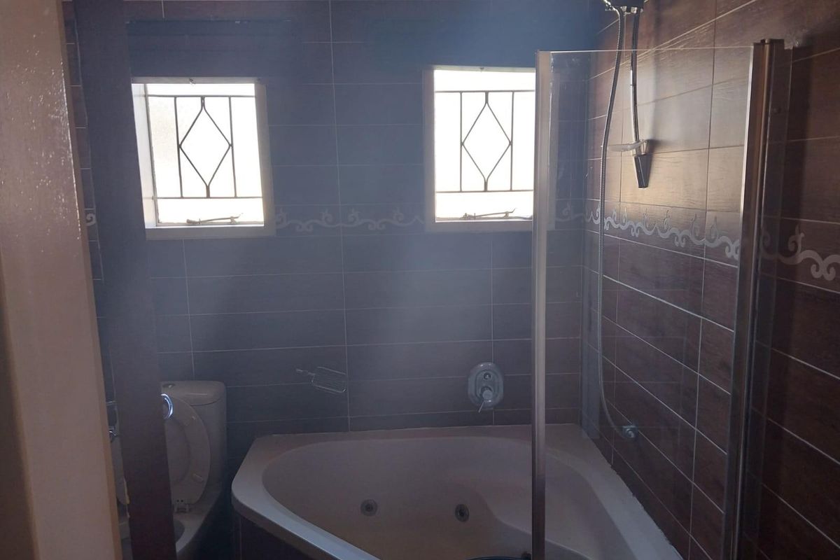A functional bathroom featuring a corner jetted bathtub, integrated shower head, and tiled wall finishes with security-barred windows.
