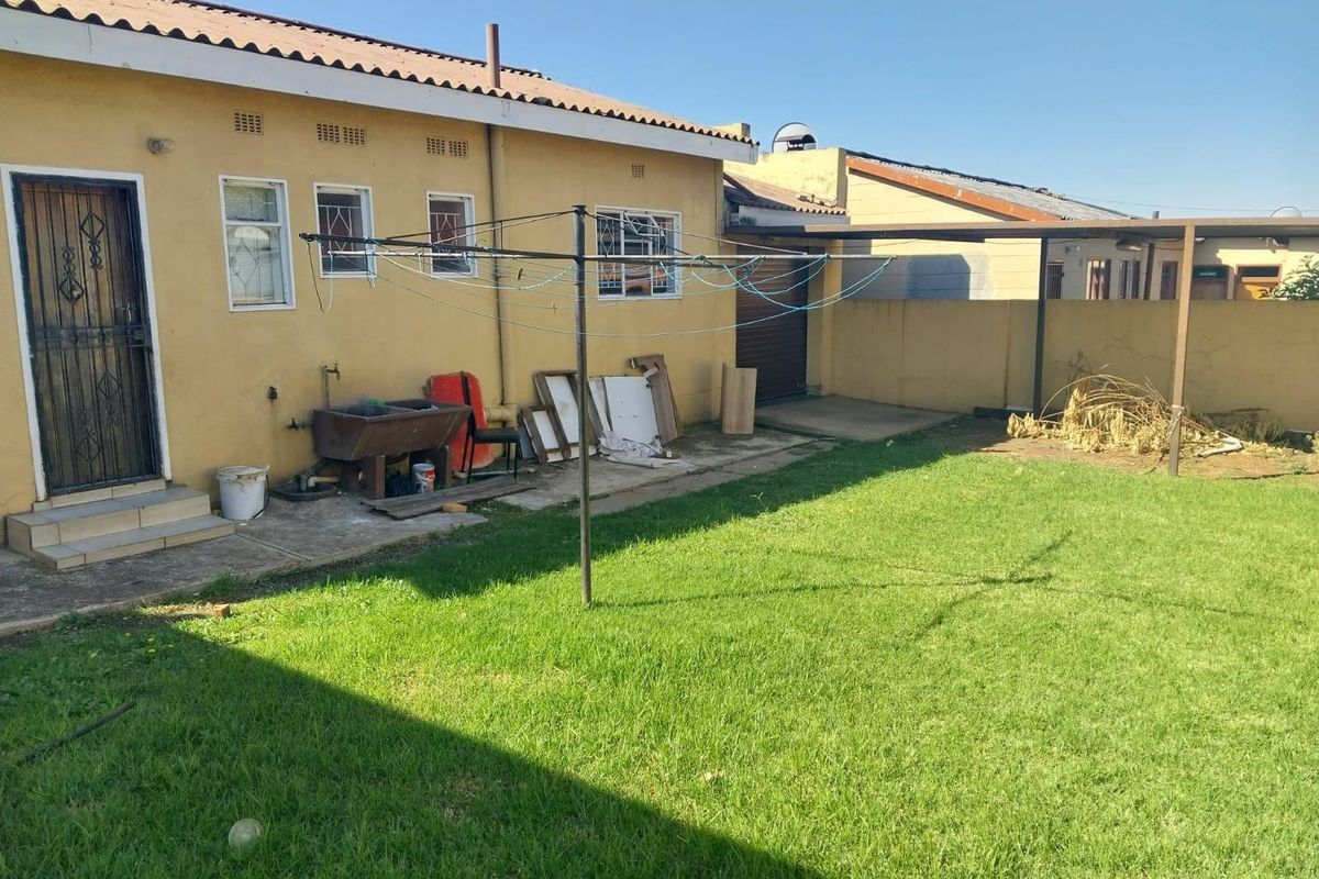Rear exterior view of the property featuring a lawn, concrete wash trough, security features, and a covered carport area.