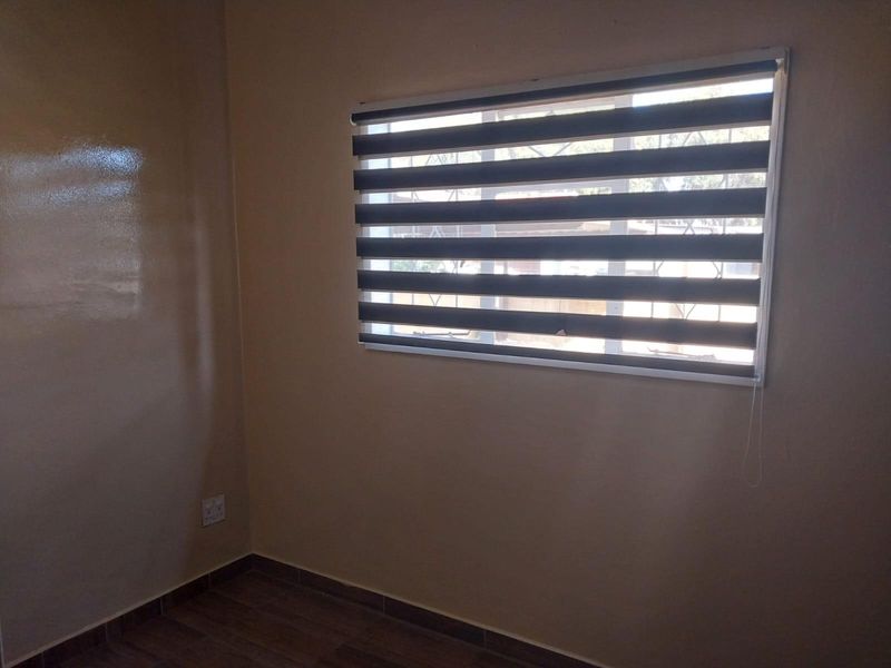 A clean, empty bedroom featuring neutral wall paint, modern zebra blinds, and wood-look laminate flooring.