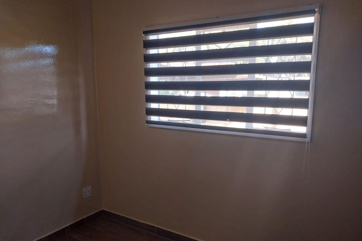 A clean, empty bedroom featuring neutral wall paint, modern zebra blinds, and wood-look laminate flooring.
