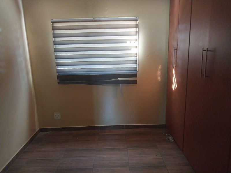 A compact bedroom featuring tiled flooring, a built-in wardrobe, and a window with fitted blinds.