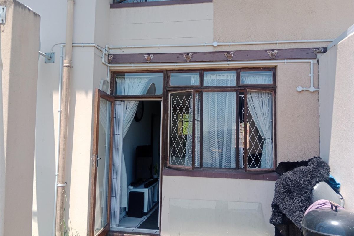 Exterior view of the rear facade featuring timber-framed windows with security bars and a single door leading into the interior living space.
