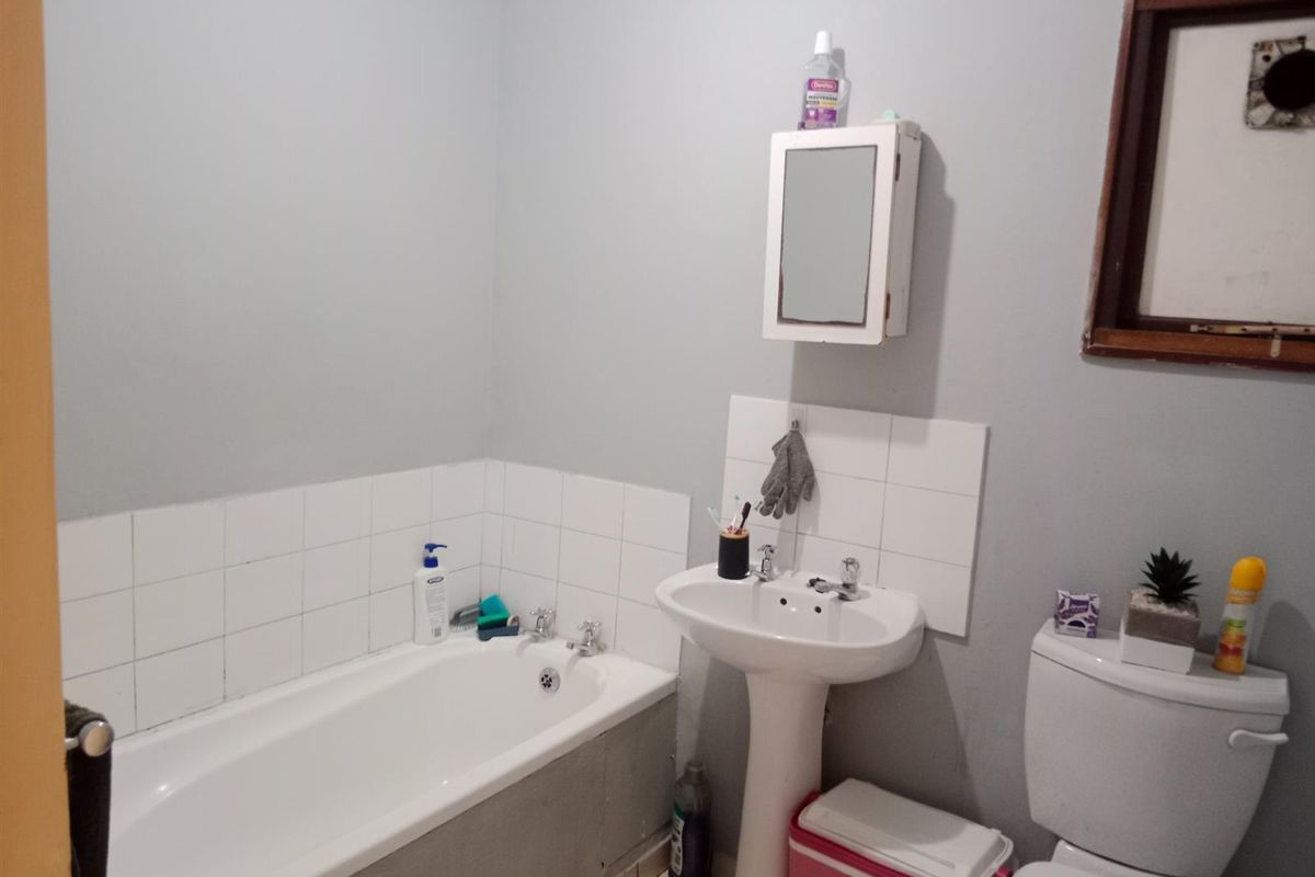 A functional bathroom featuring a standard bathtub, pedestal basin, and toilet with tiled splashbacks and a wall-mounted medicine cabinet.