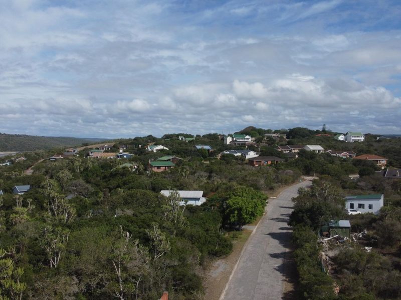 An aerial view of a residential coastal neighborhood featuring paved roads, established vegetation, and surrounding natural landscape.