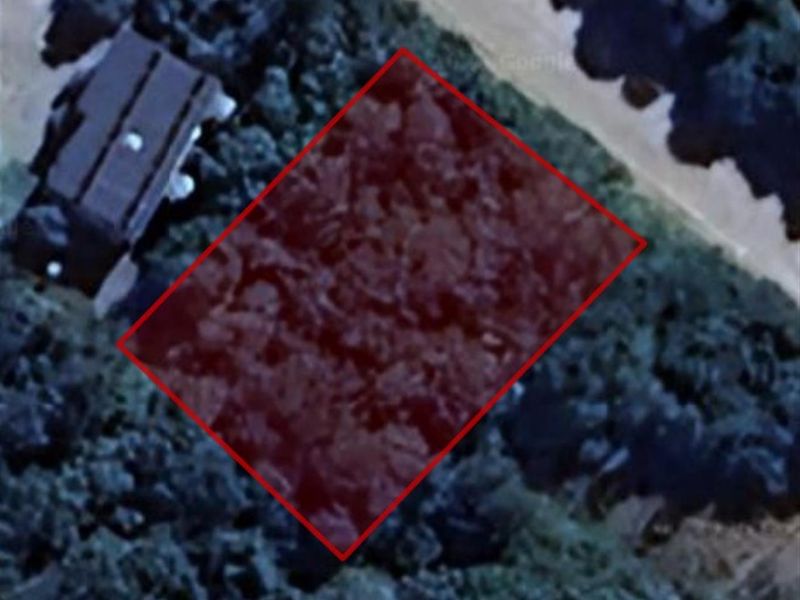An aerial view of a vacant residential plot highlighted in red, showing the surrounding vegetation and proximity to neighboring properties.