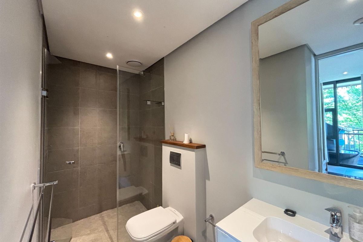 Modern bathroom featuring a walk-in shower with grey tiling, a wall-mounted toilet, and a vanity unit with a framed mirror.