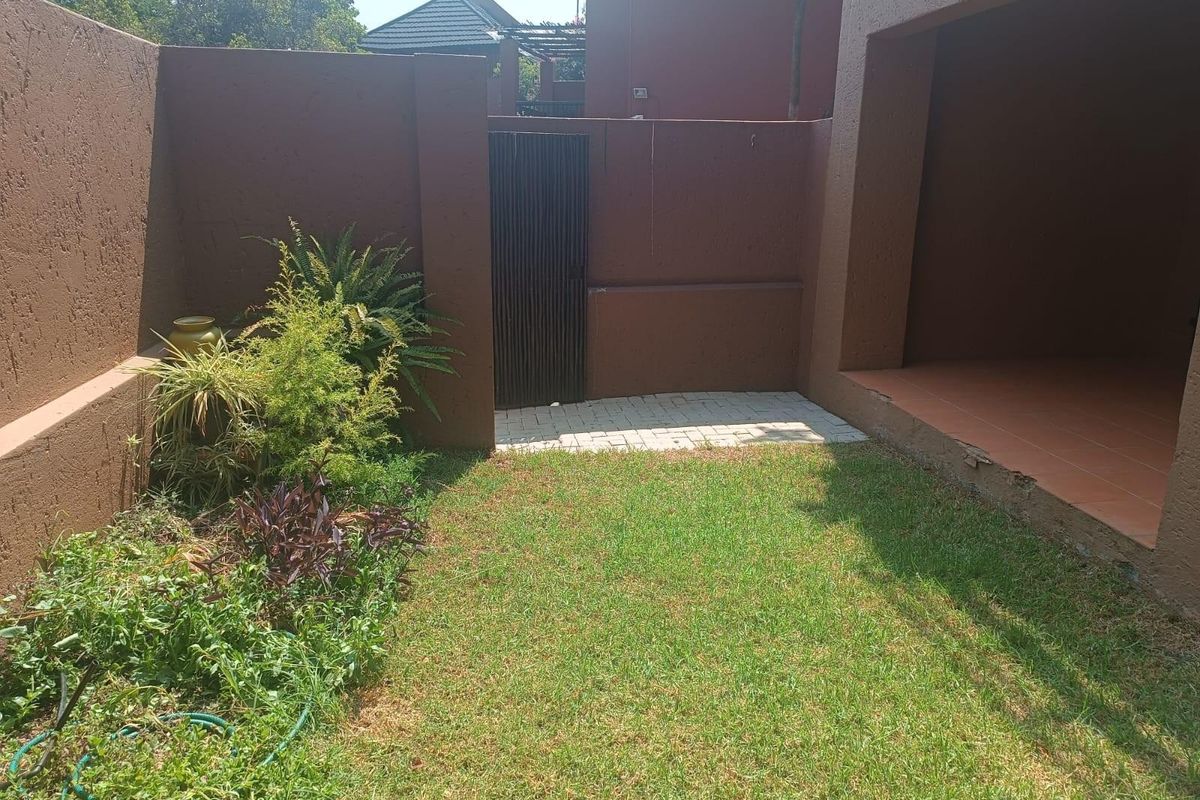 A private rear courtyard featuring a small lawn, paved walkway, metal gate, and a covered patio area with tiled flooring.