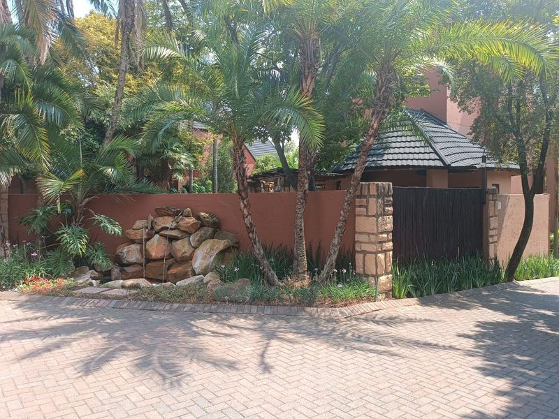 Front exterior view featuring a paved driveway, landscaped garden with a stone water feature, and a secure boundary wall with stone pillar detailing.