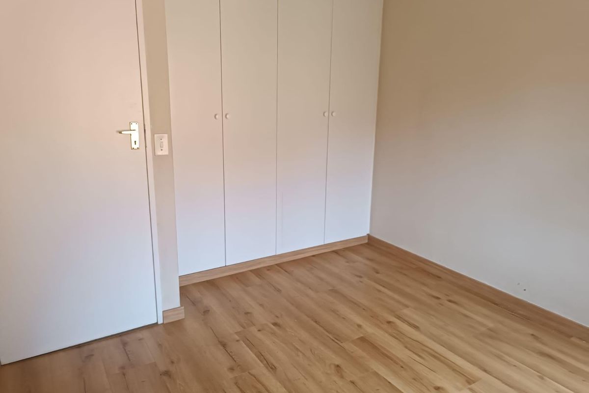 A clean, empty bedroom featuring light-toned laminate flooring and white built-in cupboards, offering a neutral canvas for personalization.
