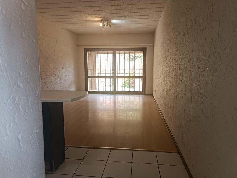 An empty open-plan living area featuring a breakfast bar, laminate and tiled flooring, and a sliding glass door with security gate access.