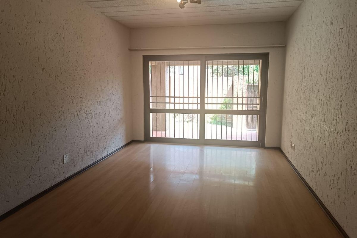 An empty living room featuring laminate flooring, textured walls, and a sliding glass door with an integrated security gate leading to the exterior.