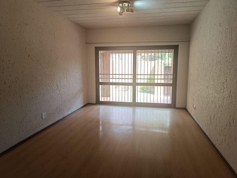 An empty living room featuring laminate flooring, textured walls, and a sliding glass door with an integrated security gate leading to the exterior.