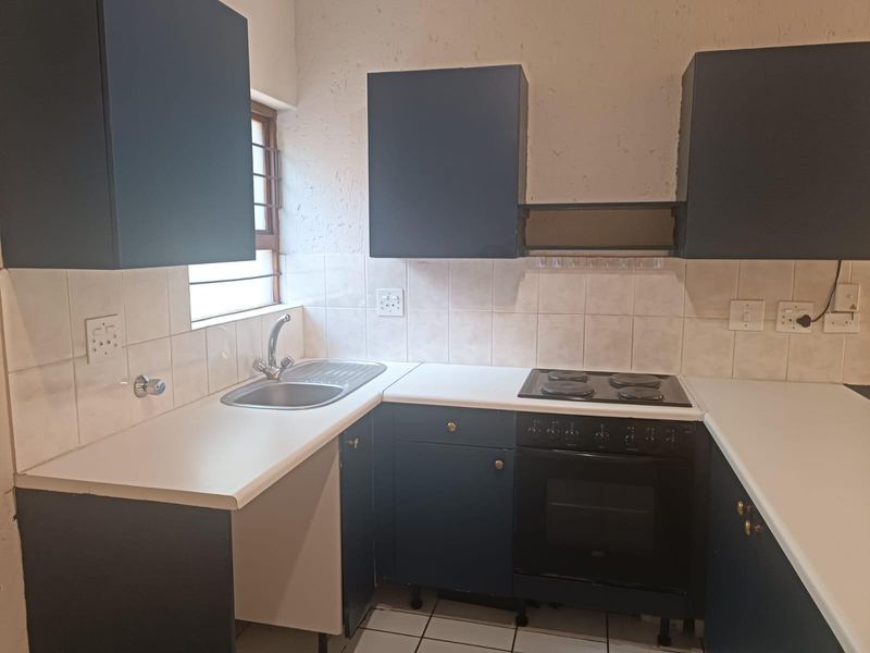 A compact kitchen featuring dark blue cabinetry, white laminate countertops, a built-in electric oven and hob, and a tiled backsplash.