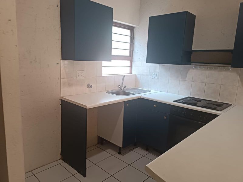 Compact kitchen featuring dark cabinetry, laminate countertops, built-in oven and hob, tiled backsplash, and tiled flooring.