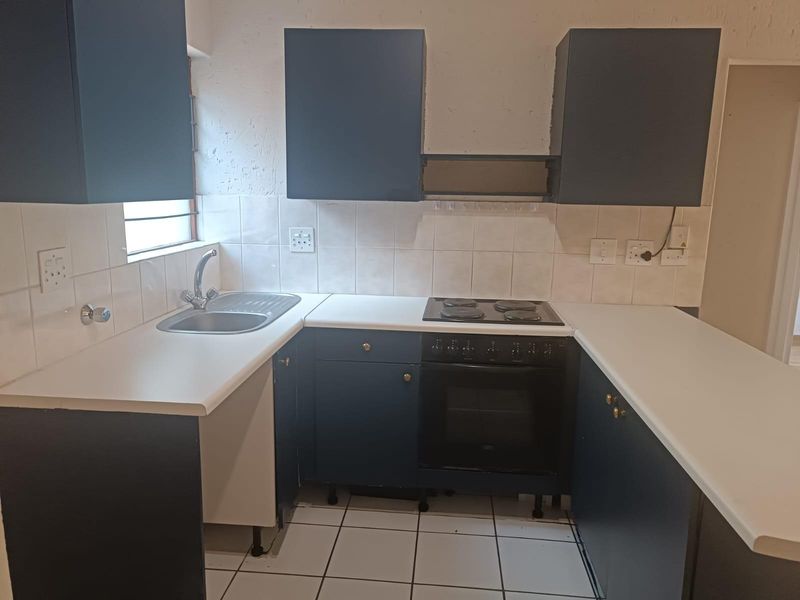 A functional kitchen featuring dark blue cabinetry, white laminate countertops, a built-in electric oven and hob, and tiled flooring.
