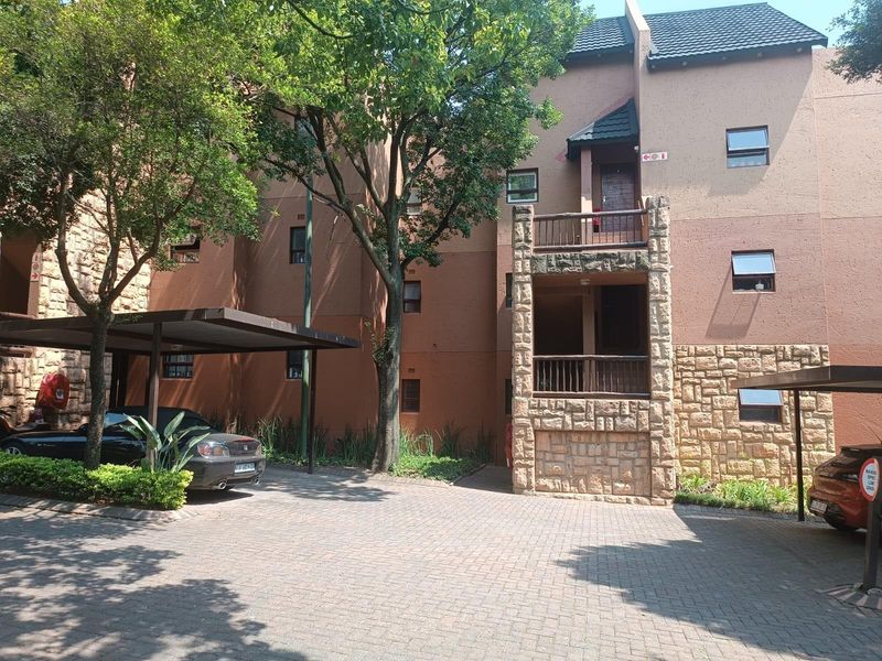 Front elevation of an apartment complex featuring stone cladding, paved parking area with carports, and private balconies.