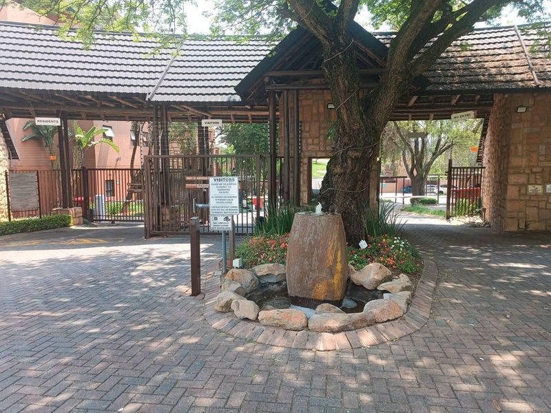 The secure entrance to the apartment complex features a paved driveway, stone-clad guardhouse, and a decorative water feature.