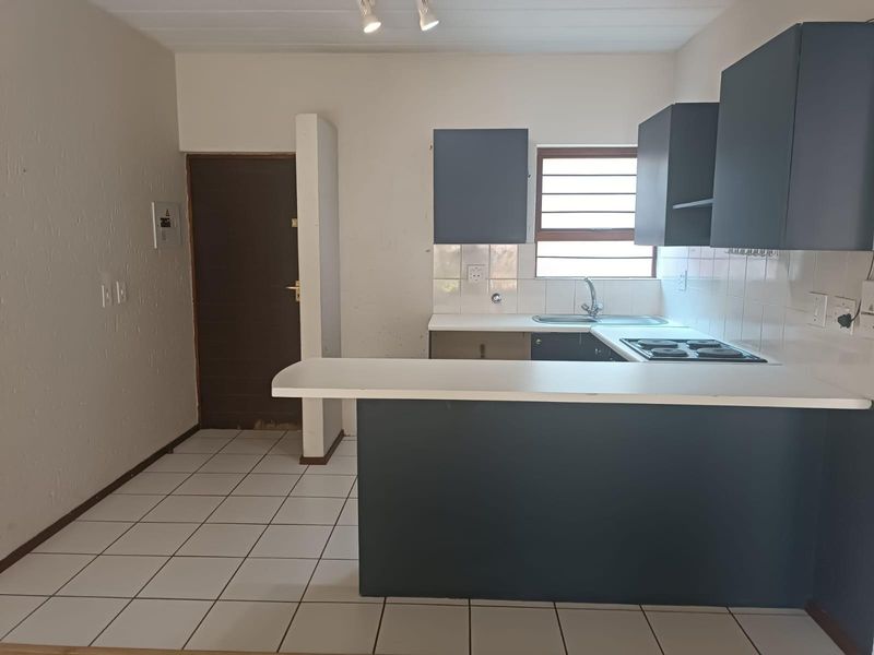 A functional kitchen featuring dark cabinetry, a breakfast bar, electric hob, and tiled flooring. The space is vacant and ready for updates.