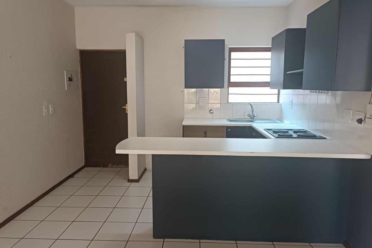 A functional kitchen featuring dark cabinetry, a breakfast bar, electric hob, and tiled flooring. The space is vacant and ready for updates.