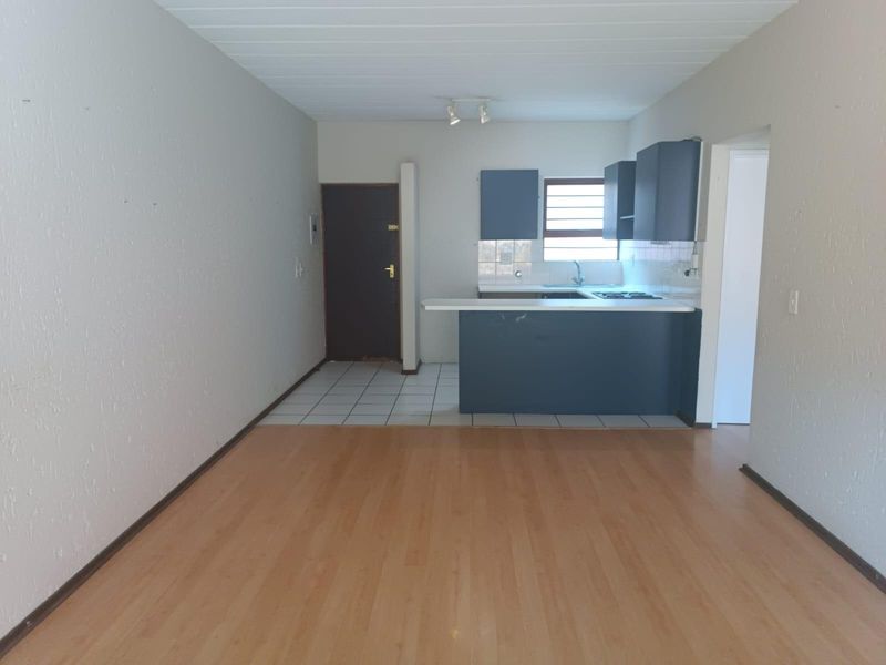 An open-plan living and kitchen area featuring laminate flooring, a breakfast bar, and built-in kitchen cabinetry in a neutral, vacant space.