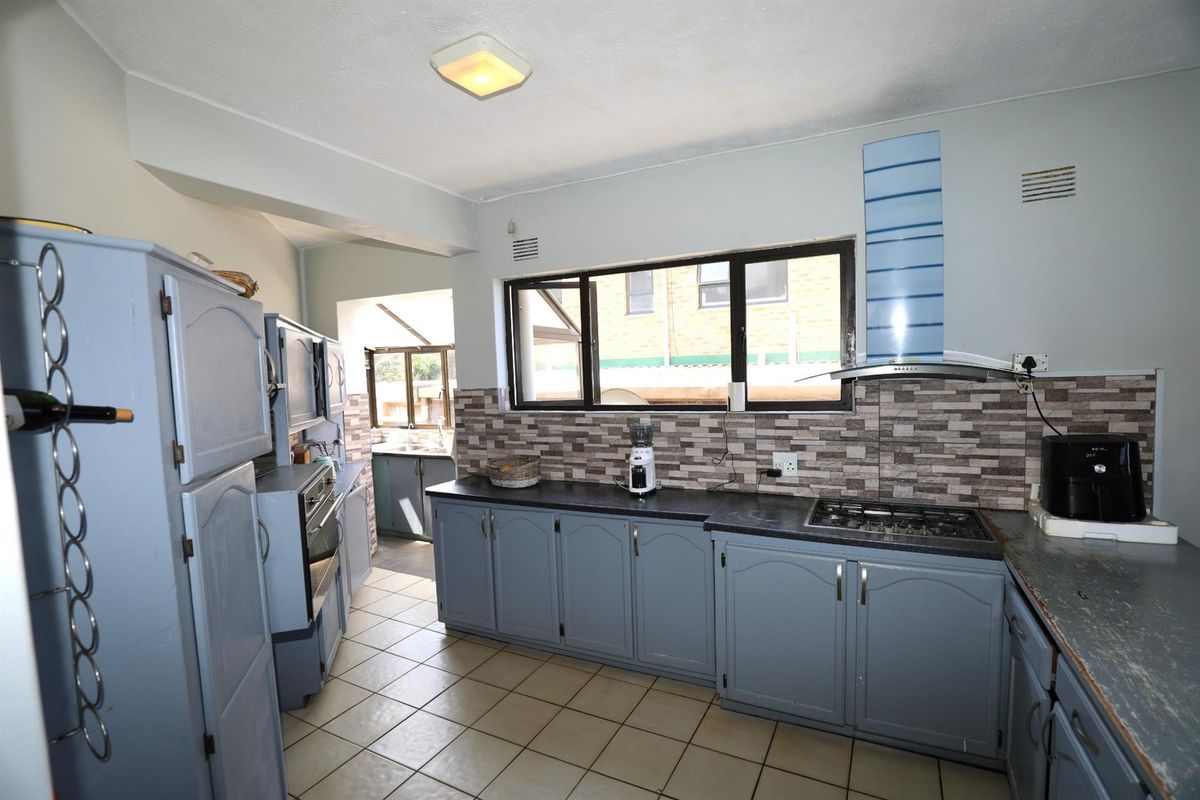 Functional kitchen featuring blue cabinetry, stone-look backsplash, built-in oven, gas hob, and extractor fan, with an adjoining scullery area.