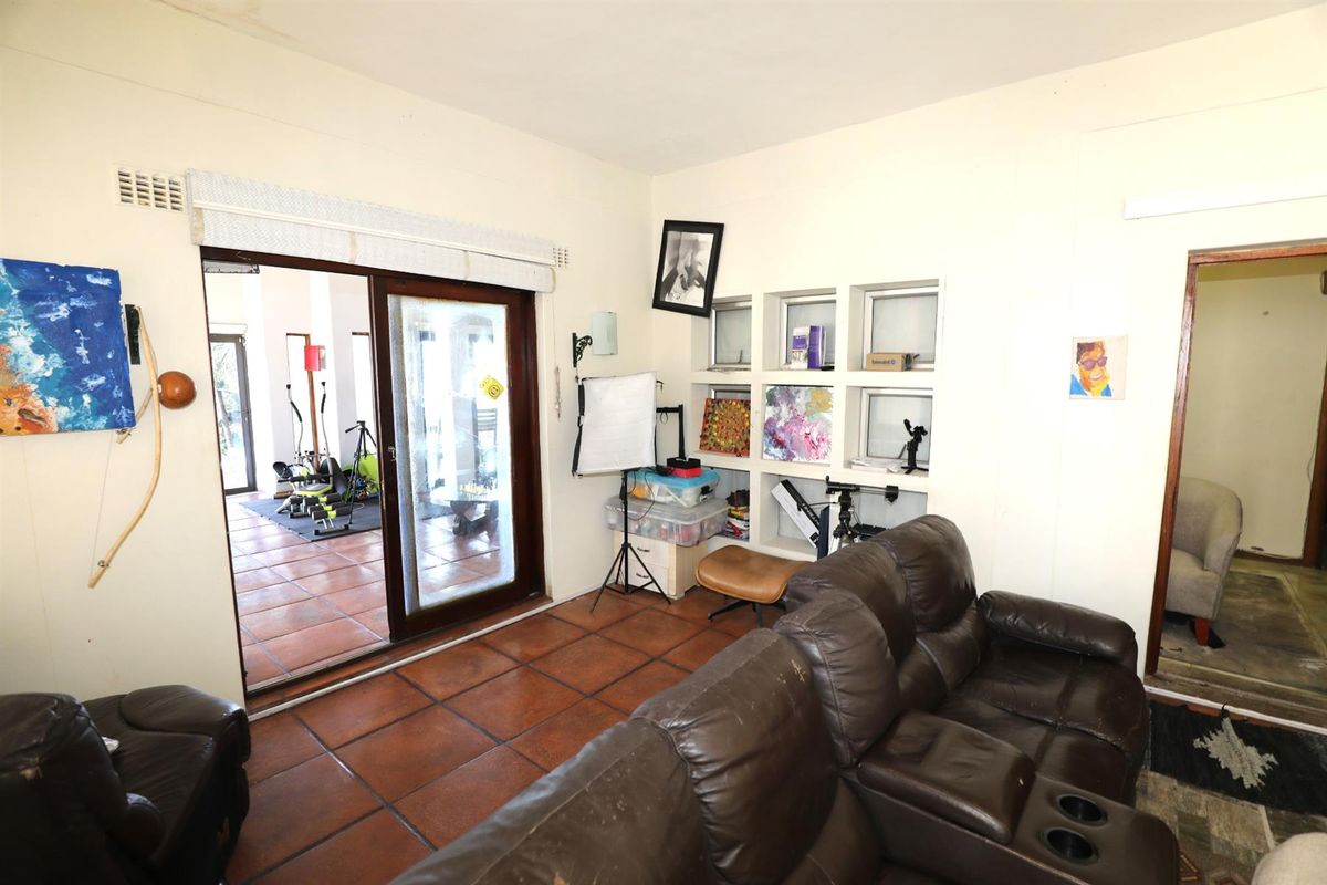 Living room featuring terracotta floor tiles, built-in wall shelving, and sliding glass doors providing access to an adjacent patio area.