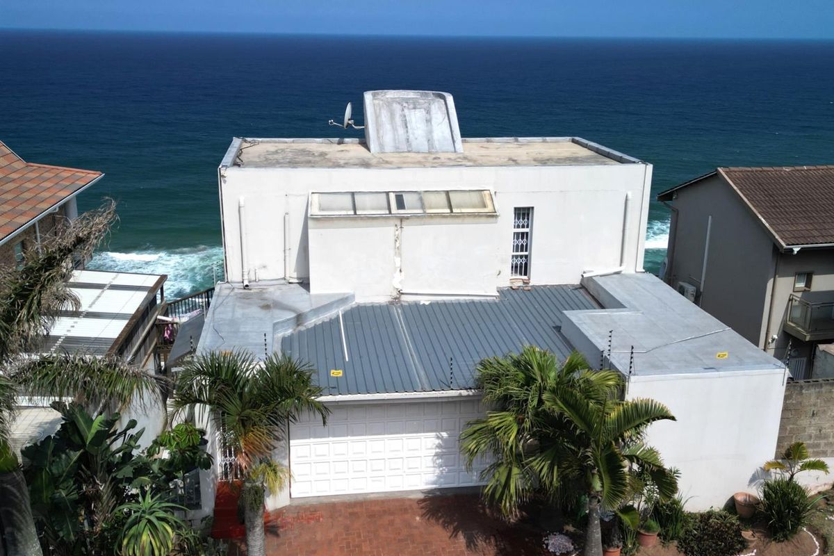 Aerial view of a coastal property featuring a flat roof, garage, and direct ocean views.