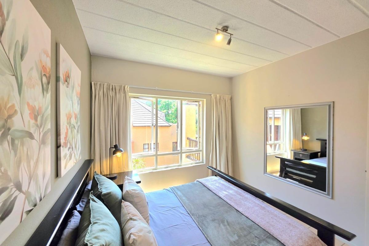 A well-lit bedroom featuring a large window, neutral wall tones, and a textured ceiling finish.