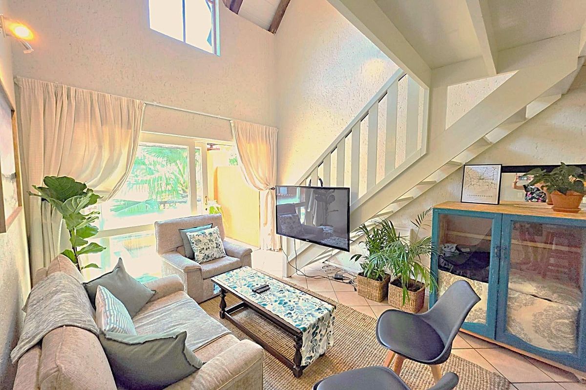 Spacious double-volume living area featuring a staircase, large windows, and tiled flooring, offering an airy and open atmosphere.