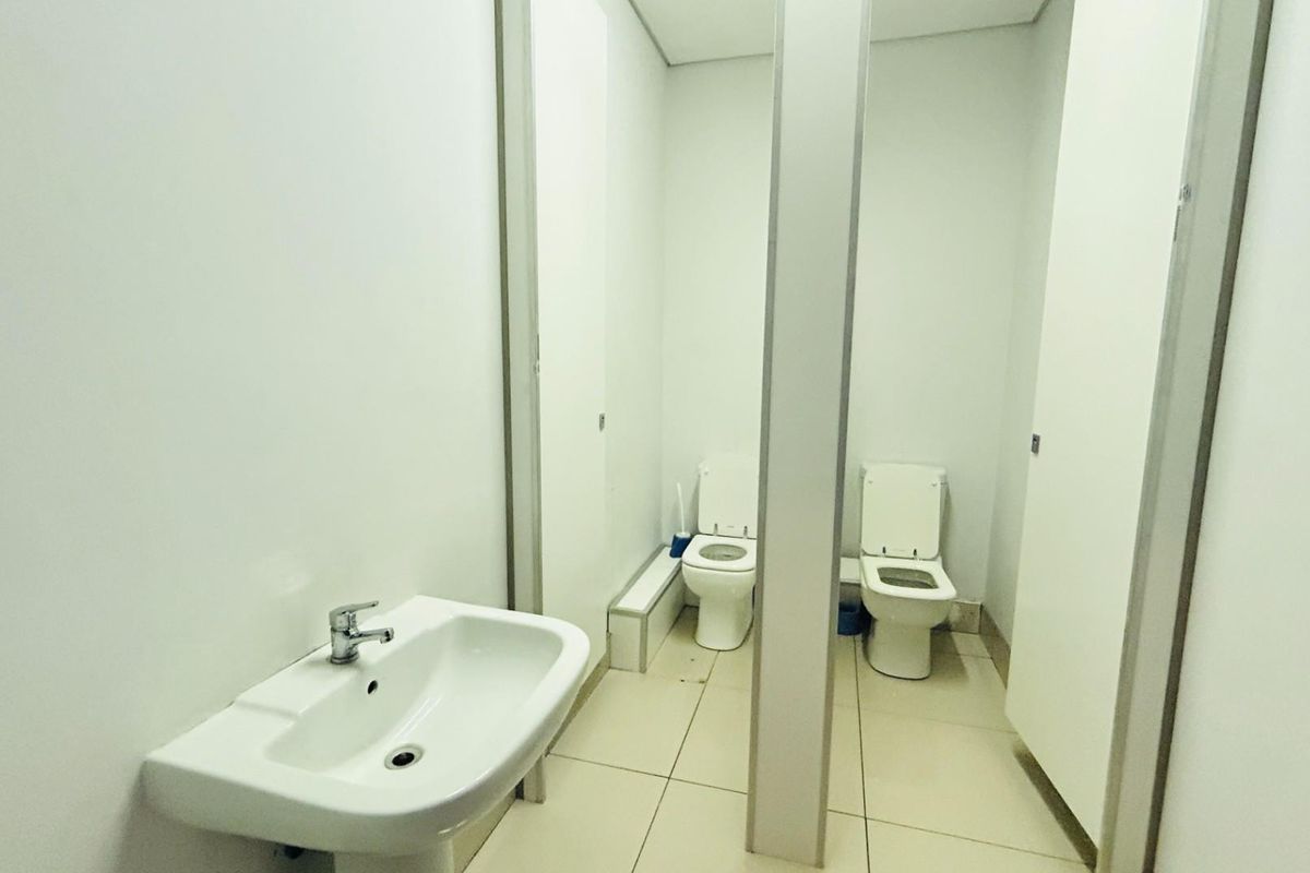 A commercial restroom facility featuring two partitioned toilet stalls and a wall-mounted ceramic washbasin with chrome faucet.