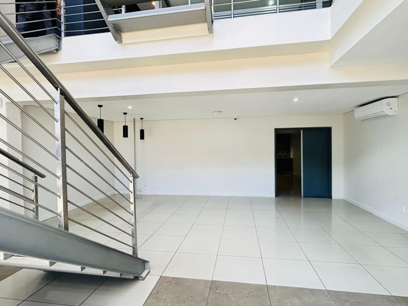 Spacious open-plan commercial interior featuring tiled flooring, a modern steel staircase with railings, and a wall-mounted air conditioning unit.