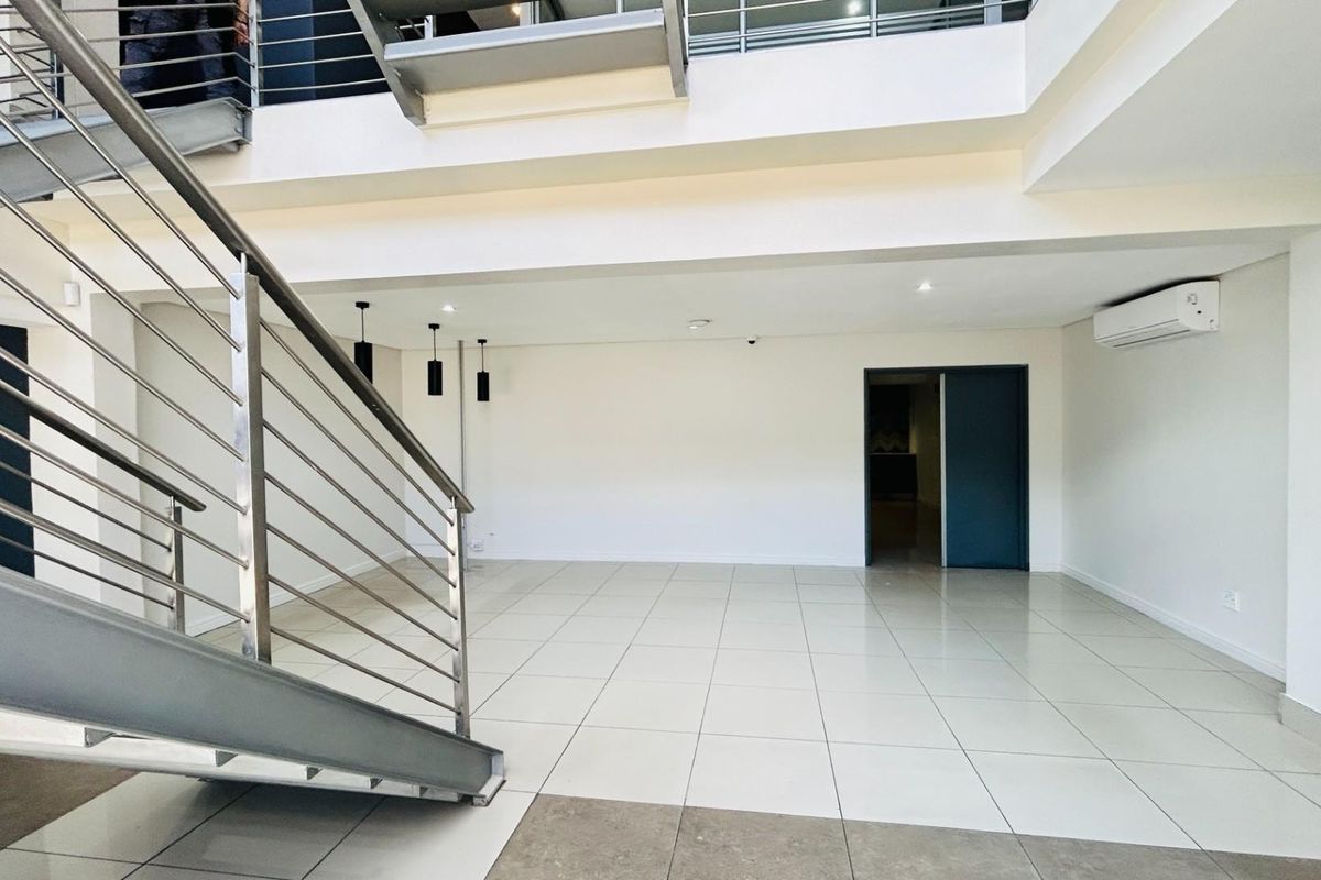 Spacious open-plan commercial interior featuring tiled flooring, a modern steel staircase with railings, and a wall-mounted air conditioning unit.