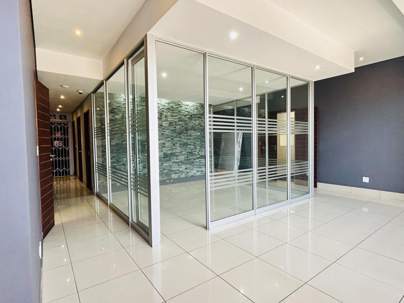 Modern commercial office space featuring glass partitioning, tiled flooring, and a decorative stone feature wall, providing a professional and bright work environment.