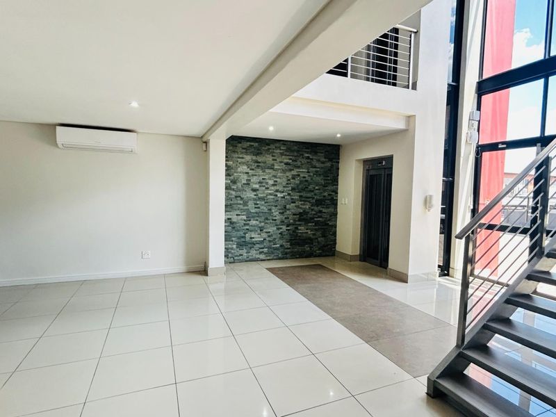Spacious commercial lobby featuring a double-volume ceiling, modern staircase, elevator access, and a decorative stone feature wall.