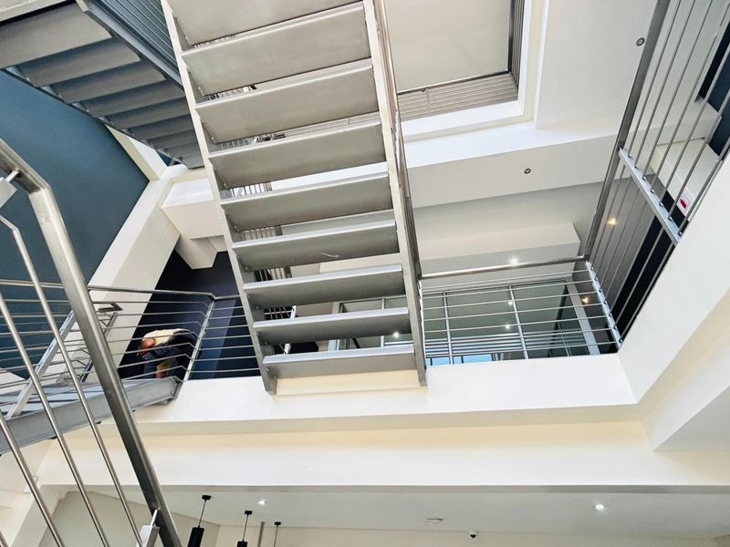 Modern commercial interior featuring a striking open-plan staircase with metal treads and stainless steel railings, connecting multiple levels with a contemporary architectural design.