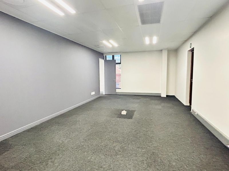 A vacant commercial office space featuring grey carpeting, suspended ceiling tiles, recessed lighting, and neutral wall finishes.