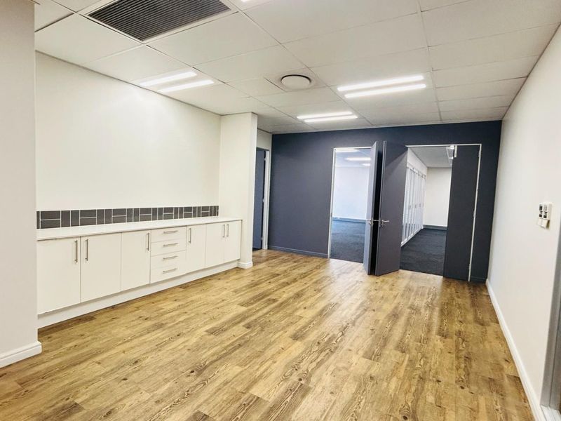 A modern, well-maintained office space featuring wood-look flooring, built-in cabinetry, recessed ceiling lighting, and a neutral color palette with a dark accent wall.
