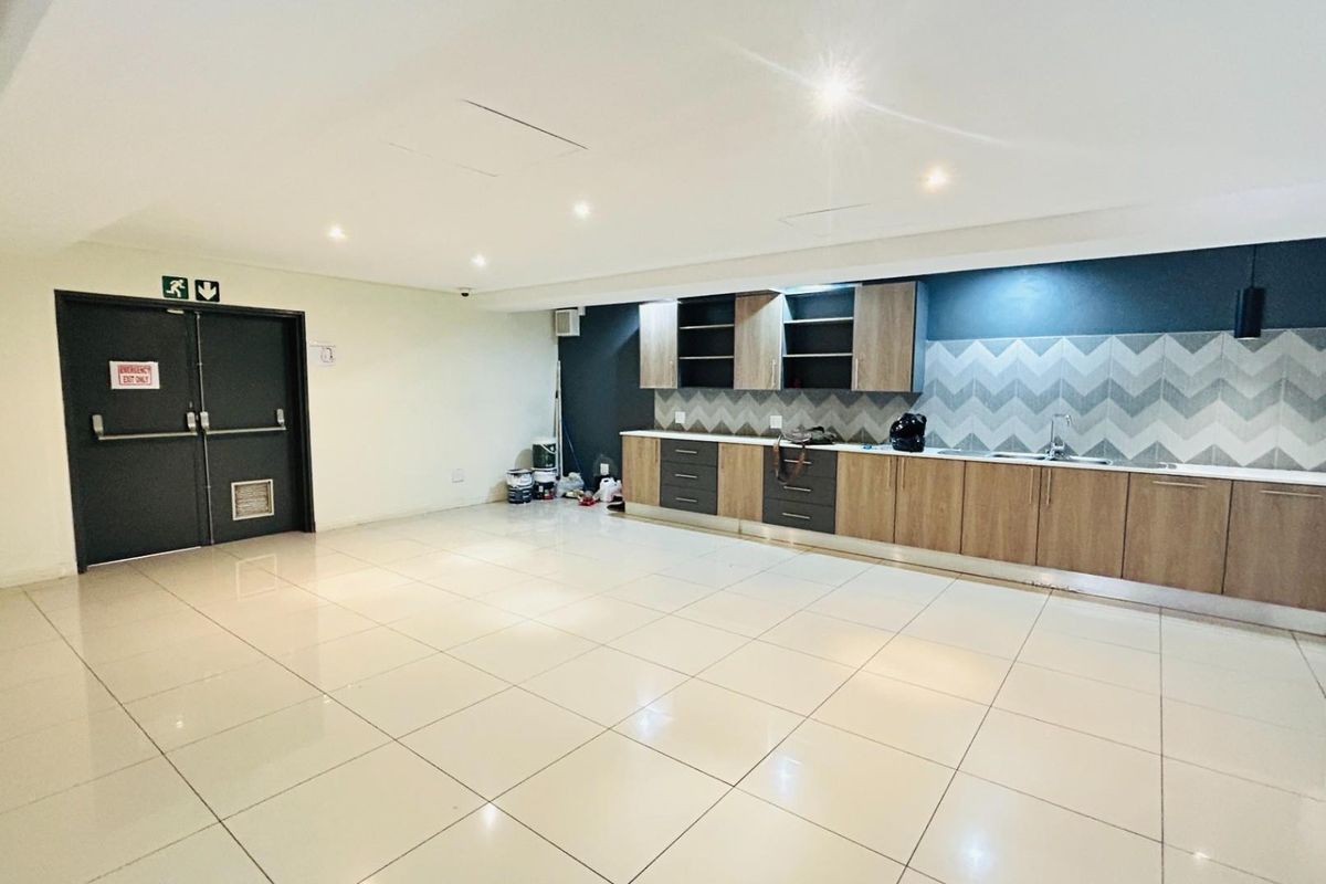 A spacious commercial kitchenette featuring modern wood-finish cabinetry, chevron-patterned backsplash, integrated sink, and tiled flooring with double emergency exit doors.