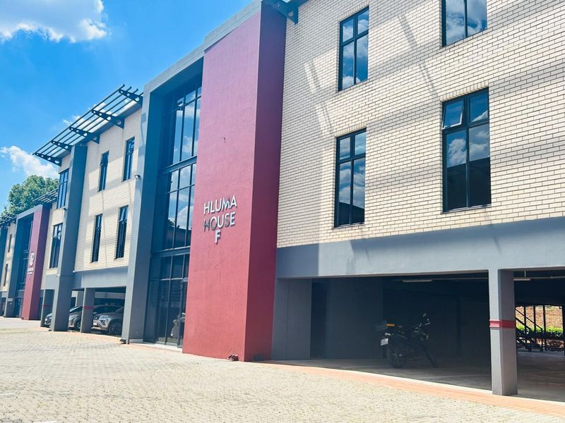 Exterior view of Hluma House F, a modern commercial building featuring brick facade, large glass windows, and covered ground-level parking.