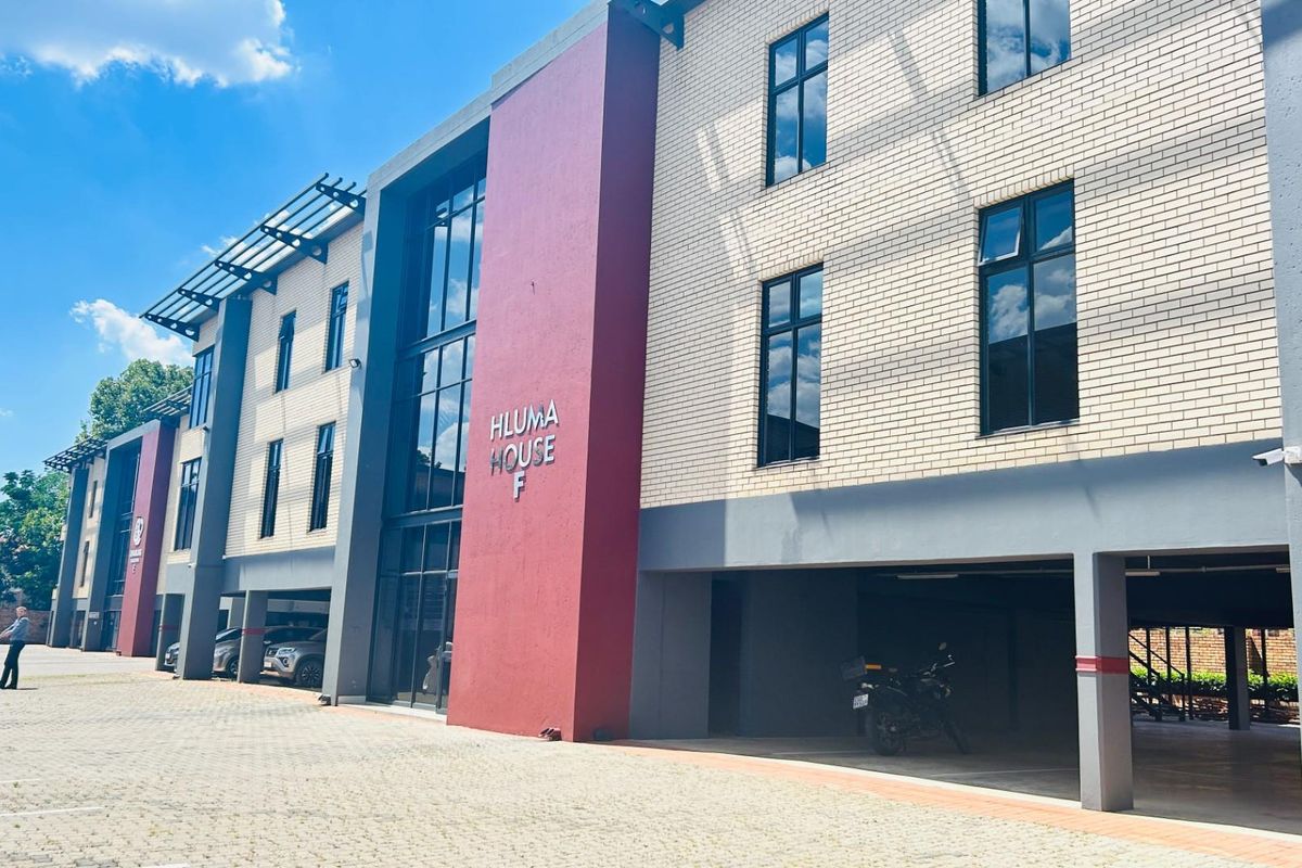 Exterior view of Hluma House F, a modern commercial building featuring brick facade, large glass windows, and covered ground-level parking.